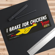 Overhead view of the I Brake for Chickens bumper sticker on a black mat beside a pen and ruler, showing its size.