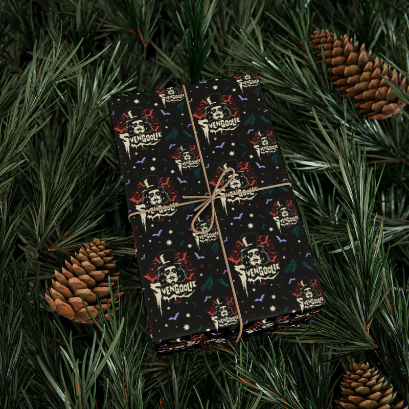 Gift box wrapped in Svengoolie wrapping paper tied with twine, resting on pine branches beside two pinecones.