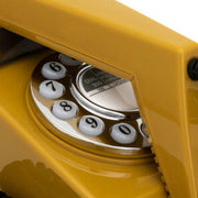 Close-up of the mustard phone's rotary dial showing the numbers 6 through 0 beside a chrome center plate