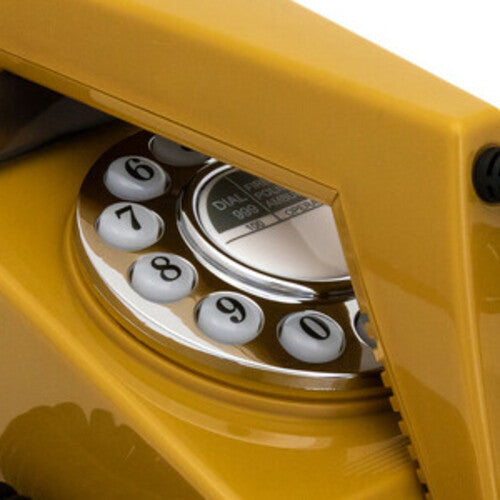 Close-up of the mustard phone's rotary dial showing the numbers 6 through 0 beside a chrome center plate