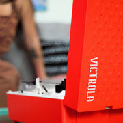 Close-up of red record player's upright lid edge with white 'VICTROLA' text running vertically down the side.