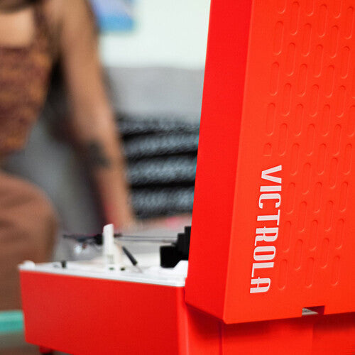 Close-up of red record player's upright lid edge with white 'VICTROLA' text running vertically down the side.