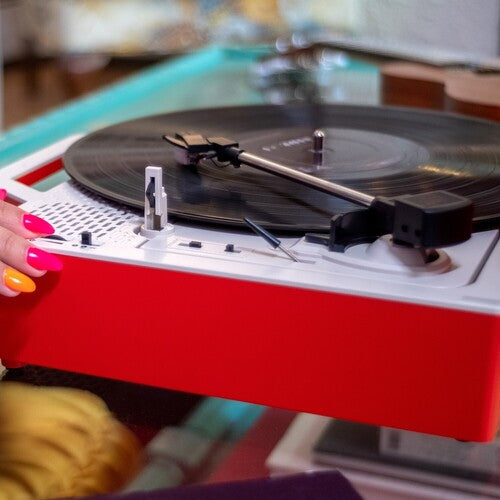 Close-up of red and white record player with a black vinyl record and tonearm, as a hand with pink nails rests at the left edge.
