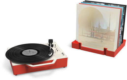 Red record player beside a red stand holding a row of vinyl albums in its slots, with a black record on the platter.
