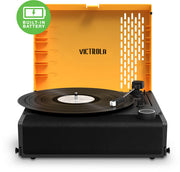 Orange and black Victrola Revolution GO portable record player with open lid featuring the Victrola logo with the text 'VICTROLA' in black on the lid, and a built-in battery badge.