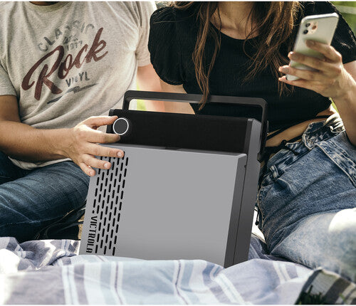 Two people sitting outdoors holding the gray record player on their laps, with the man wearing a gray Rock Vinyl graphic t-shirt