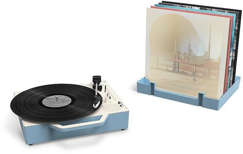 Turntable from the Victrola Re-Spin with a black record, shown beside a light blue record stand holding albums in sleeves.