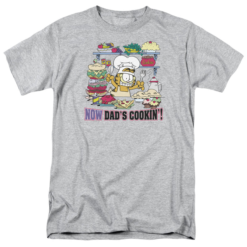 Heather gray t-shirt featuring Garfield in a chef's hat and apron with food on shelves and the text 'NOW DAD'S COOKIN'!' in purple and black below.