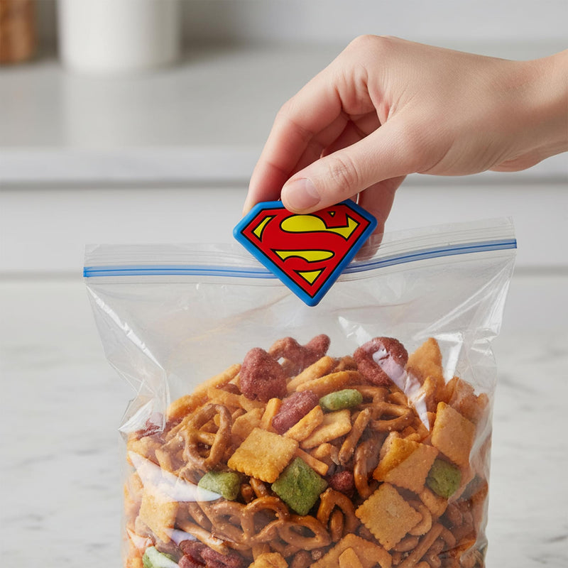 Hand using a Superman shield bag clip to seal a zipper bag of snack mix.