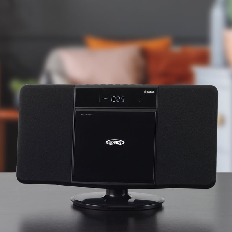 Lifestyle shot of the black Jensen music system on a tabletop in a living room, showing the front panel and digital clock.