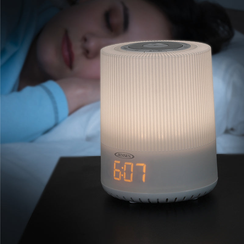 Person sleeping beside the Jensen mood lamp clock radio glowing warm white on a nightstand, showing amber digital time 6:07