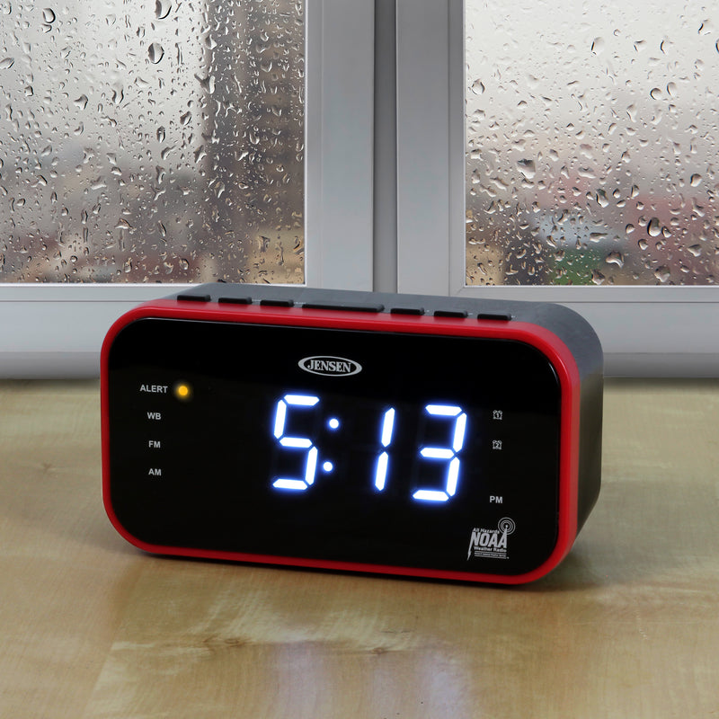 Jensen clock radio on a wooden table in front of a rainy window, showing a blue LED display and an amber ALERT light lit.