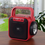 Red Jensen portable radio on a wooden table near a window, showing the front control panel with the Bluetooth label and the side flashlight.