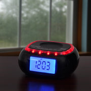 Jensen clock radio on a wooden table by a window, with the blue display showing 12:03 AM and the red LED alert ring glowing.