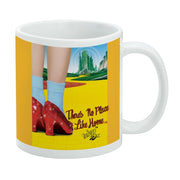 White mug featuring ruby slippers and blue socks on a yellow brick road with the text 'There's No Place Like Home' in red script on the right.