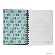 Open black Donkey Kong notebook showing a light blue patterned inside cover beside lined pages with a faint 'DONKEY KONG' logo.