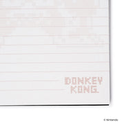 Close-up of a lined page corner with faint pixel artwork and a small red 'DONKEY KONG' logo in the lower right.