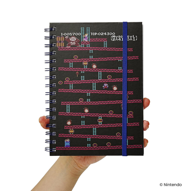Notebook held in a hand showing the black Donkey Kong arcade cover with blue elastic closure for scale.