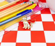 Close-up of Krypto enamel pin on a red and white checkered surface beside a clear case of colored pencils.