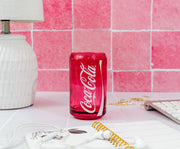 Styled shot of the red Coca-Cola glass cup on a pink-tiled desk beside a lamp, keyboard, and notebook, showing the white Coca-Cola script logo.