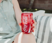 Close-up of a hand holding the red Coca-Cola glass cup, showing the white Coca-Cola script logo and wave stripe.