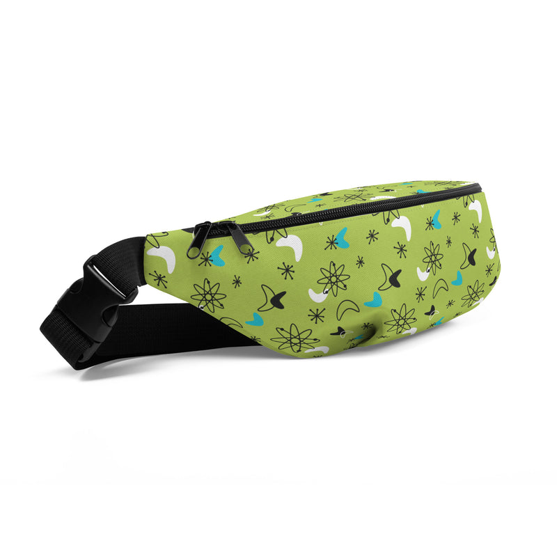 Angled view of lime green fanny pack featuring a retro atomic pattern of black atom symbols, starbursts, and white and teal boomerang shapes, with a black zipper and buckle strap.