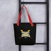 Black tote bag with red handles hanging on a black ladder, featuring two crossed yellow chickens with red combs and the text 'Official Chicken Thrower' in white above a small MeTV logo.