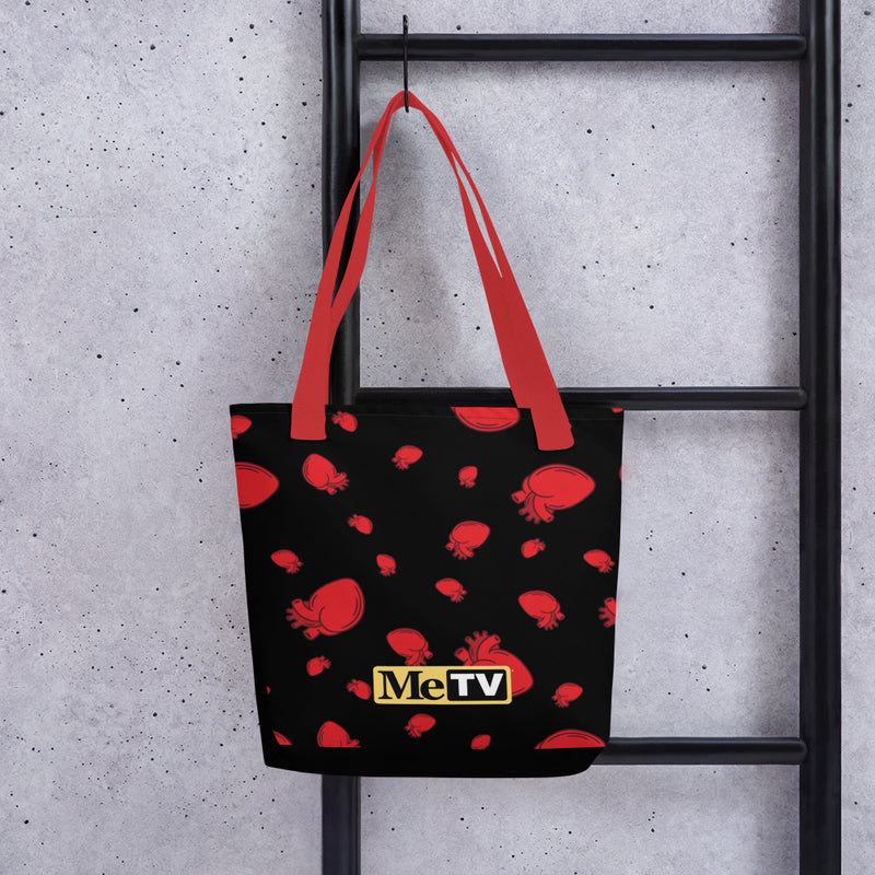 Black tote bag with red handles featuring an all-over pattern of red anatomical hearts and a small yellow MeTV logo near the bottom center.