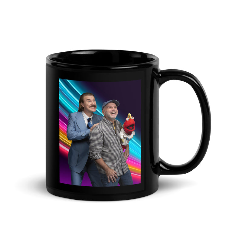 Front view of black glossy ceramic mug featuring a color photo of two men and a red puppet on a colorful striped background