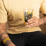 Person holding the Svengoolie pint glass filled with an amber drink, showing the monster illustration against a pale yellow shirt.