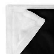 Close-up of a folded corner of a black and white plush throw blanket showing a white sherpa-style reverse side and black fleece front.