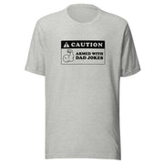 Heather gray t-shirt featuring a black caution sign graphic with the text 'CAUTION' and 'ARMED WITH DAD JOKES' beside a flexing arm icon.