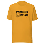 Mustard yellow t-shirt featuring a black caution sign graphic with the text 'CAUTION' and 'ARMED WITH DAD JOKES' beside a flexing arm icon.