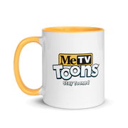 White ceramic mug with yellow handle and blue interior featuring the MeTV Toons logo with the text 'Stay Tooned' in black below it.