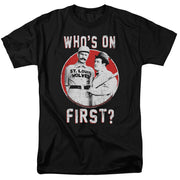 Black t-shirt with white text "WHO'S ON FIRST?" above and below a red circle showing two men in vintage baseball and suit attire.