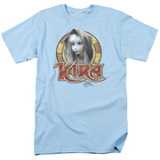 Light blue t-shirt with circular graphic of Kira, a pale puppet character in a hood, above red 'KIRA' logo text and small 'The Dark Crystal' text.