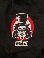 Close up view of Black polo shirt with small embroidered Svengoolie logo on chest: "MeTV" logo below.
