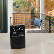Black Jensen AM/FM pocket radio with extendable antenna, speaker grille, and dial marked AM and FM, on a wooden table.