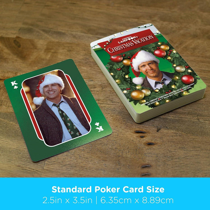 Close-up of a king of clubs card from Christmas Vacation playing cards showing Clark Griswold smiling in a Santa hat, next to the card deck.