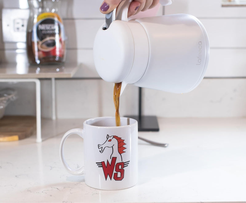 White ceramic mug with a red horse head and red 'WS' logo, being filled with coffee from a white carafe.