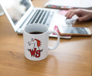 White ceramic coffee mug with a red and black horse head logo above the letters 'WS' with wing accents, filled with coffee on a wooden desk.