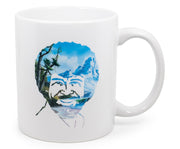 White ceramic mug with a printed portrait of Bob Ross's face formed from a landscape of mountains, trees, and a lake in blue and green tones.