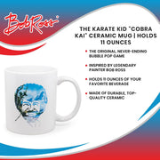 White ceramic mug with a Bob Ross portrait printed on it, his face outlined in a blue sky, snowy mountain, and tree landscape
