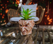 Freddy Krueger face planter with artificial succulent set on a wicker-style glass table outdoors, with a cushioned chair behind it.