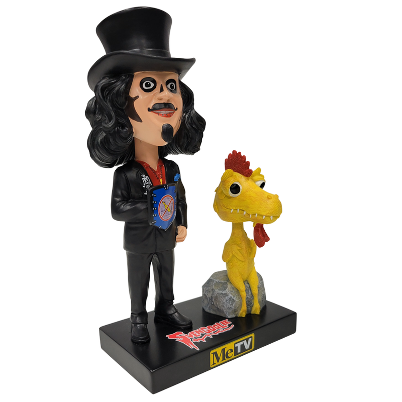 Left facing 3/4 view of Svengoolie bobblehead in black top hat, black suit, and blue shield with red emblem, beside yellow Kerwyn bobblehead on gray rock; base reads "Svengoolie" and "MeTV".