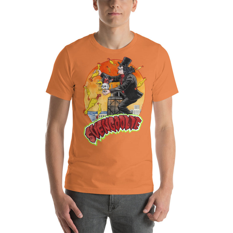 Orange tee with Svengoolie in top hat and black suit, at the top of a skyscraper, holding a skull, surrounded by rubber chickens, with 'SVENGOOLIE' in red letters over an orange sunset city.