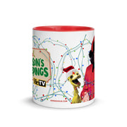 Side view of White mug with red interior: yellow puppet in Santa hat, man in red robe, string lights, and 'SVENGOOLIE.COM'.